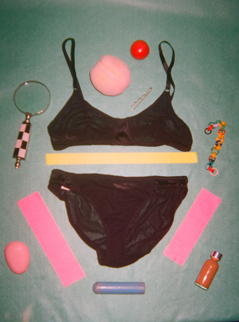 Accessories displayed around, with a black bralette and a black panty