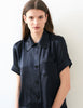 Close up, woman wearing navy silk collared short-sleeved sleep shirt with left breast pocket and contrast piping 