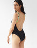 Side view of A woman wearing a black one piece swimsuit with braided straps.