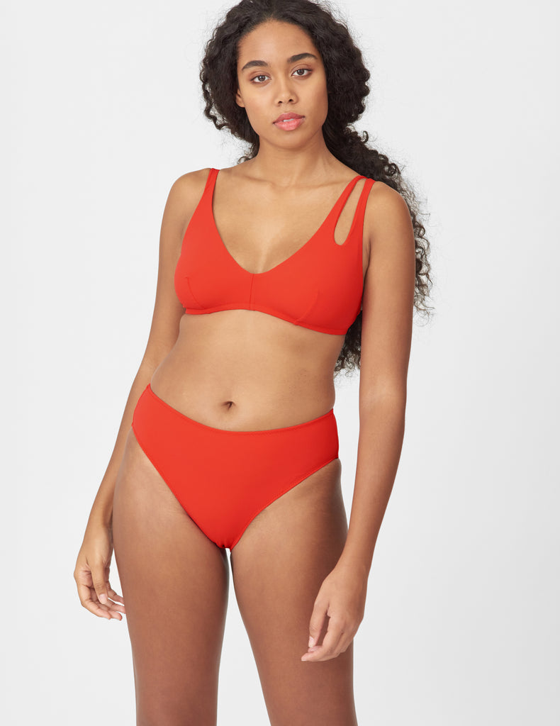 Front view of woman wearing a red bikini top with asymmetric crisscross straps with matching bottoms