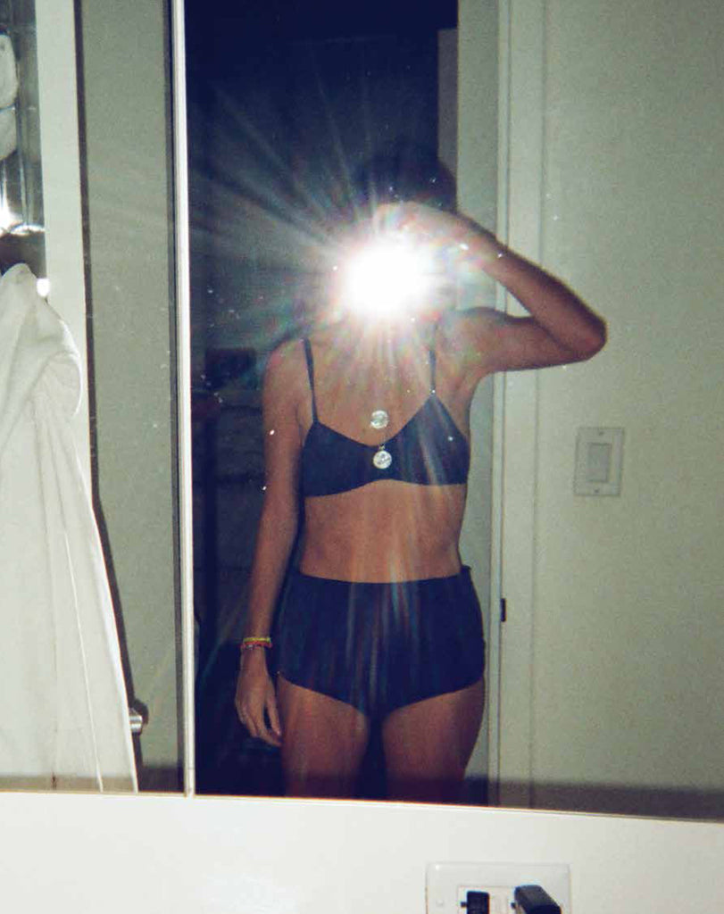 Woman takes a mirror photo, wearing black high-waisted panty, and matching bralette