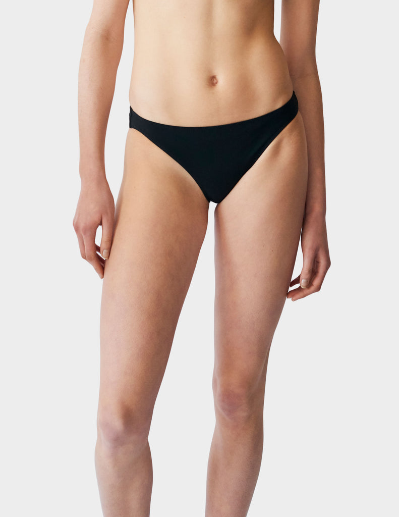 Woman wearing low-rise black swim bottoms.