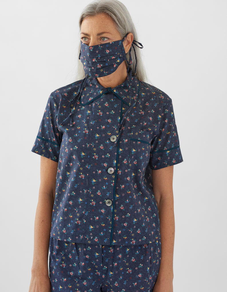 woman wearing navy floral pajama top and matching shorts and face mask