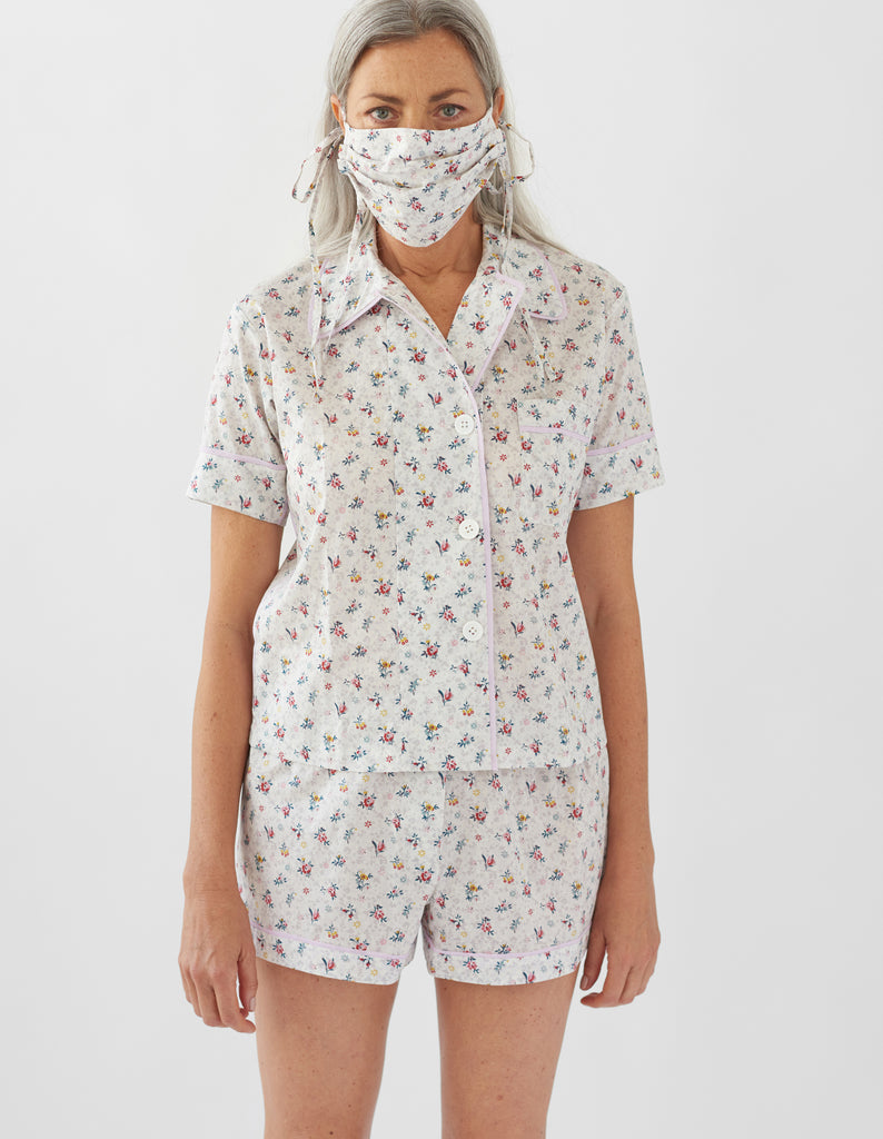 Woman wearing white floral print pajamas and Cotton face mask made from printed fabric. The design is white with red and yellow flowers