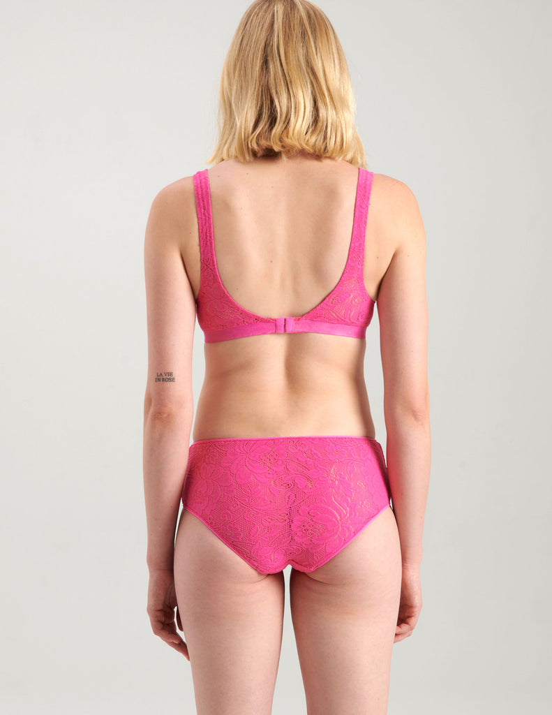 Backview of A woman wearing a bright pink lace bralette and panty.