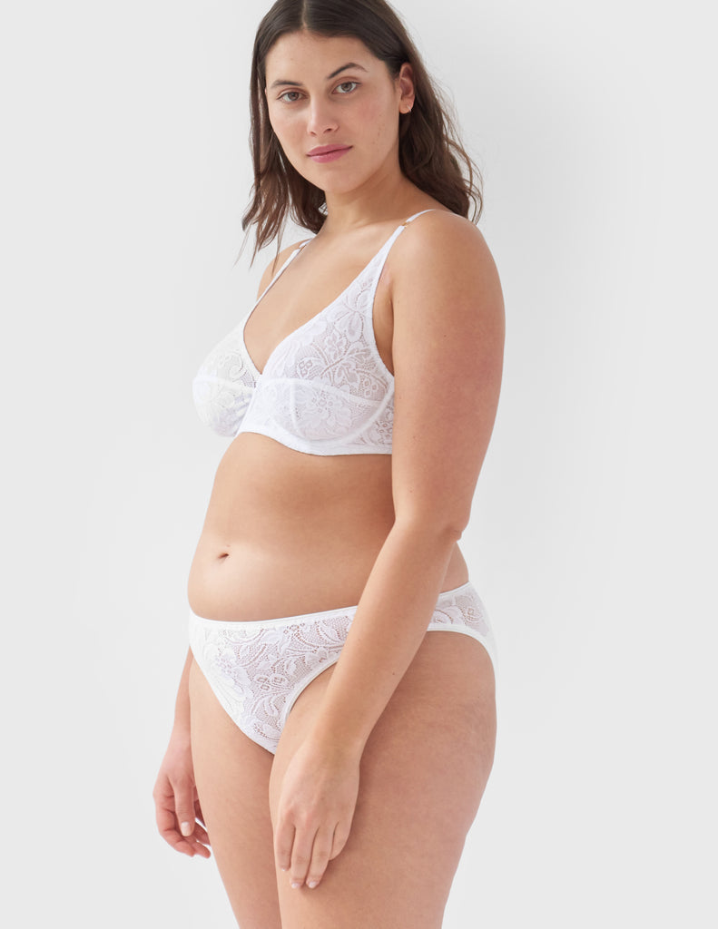Side view of woman wearing white, lace underwire bra and matching mid-rise panty.