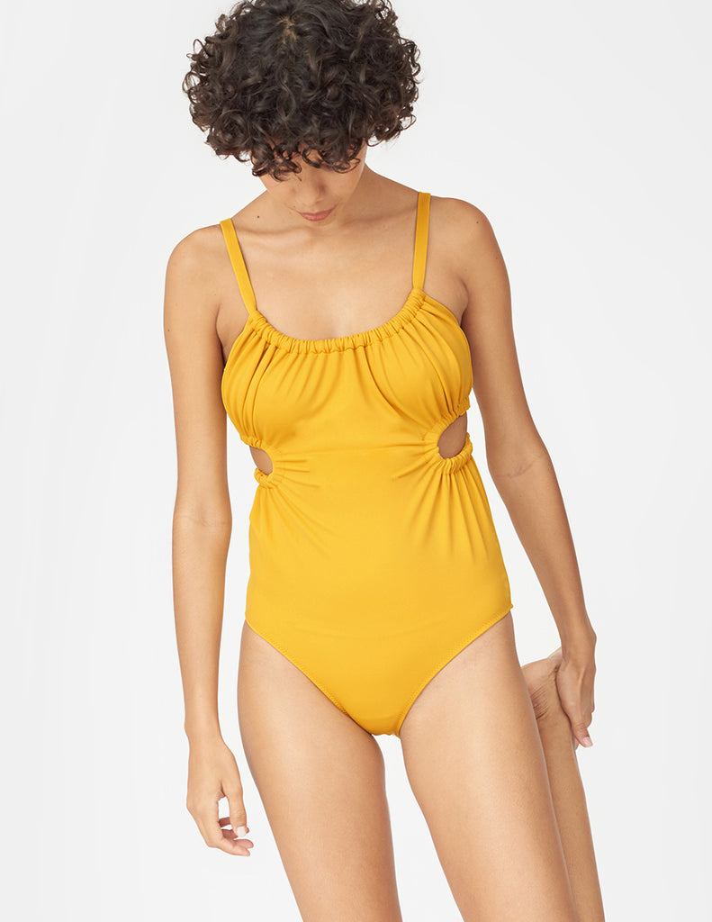 Front view of woman wearing a yellow one piece swimsuit with side cut outs and a tie in back