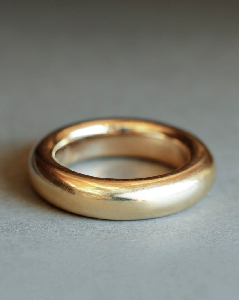 Large 18k solid yellow gold donut ring on gray paper. By George Rings. Dominus Band Grande