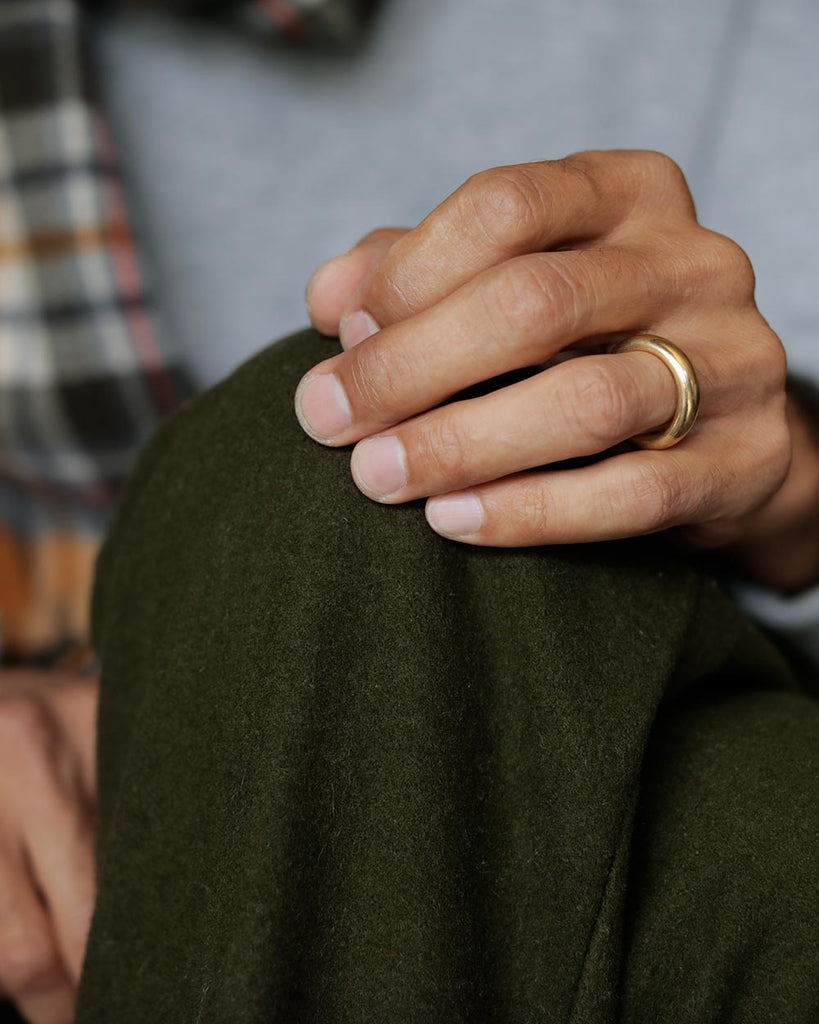 Man's hand on his green wool pants, with a Large 18k solid yellow gold donut wedding band on his ring finger