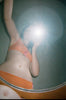 Woman takes a mirror photo, wearing orange with pink panel bralette and matching panty