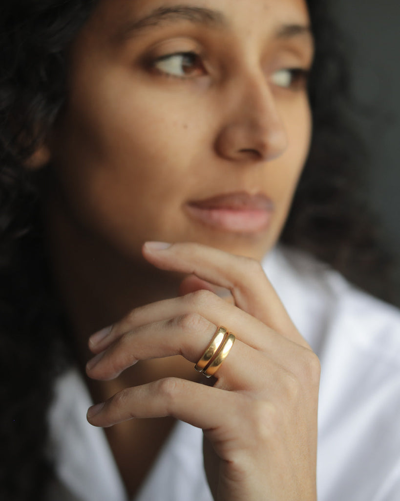 Detail shot of brown woman wearing two solid 18k yellow gold simple wedding bands stacked on ring finger. 3.5mm tall. Essential Band by George Rings.