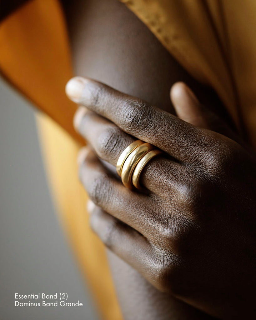 Black woman in silk dress wearing a stack of three solid 18k yellow gold simple women's wedding bands. 3.5mm tall. Essential band and Dominus Band Grande by George Rings.