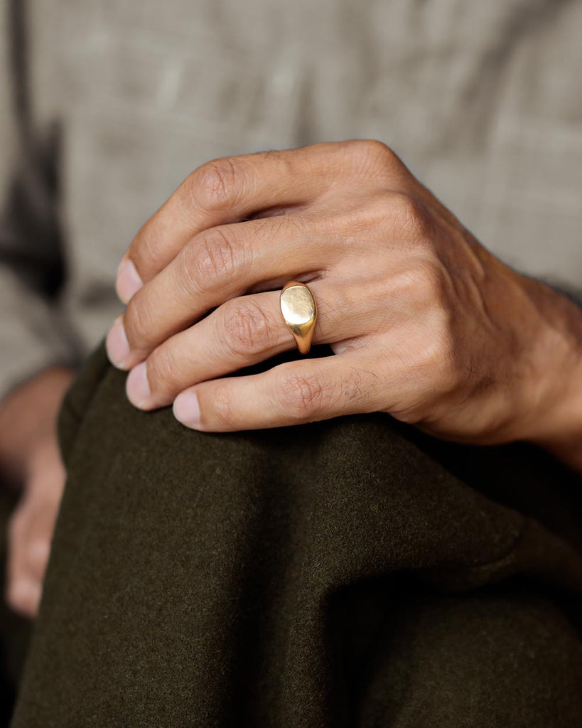 Man's hand on his green wool pants knee, wearing Solid 18k yellow gold heavy signet mens wedding band on his ring finger. Hugo Signet Ring by George Rings.