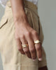Woman holds hand in front of her. Two solid yellow 18k gold rings on her hand. She wears Solid 18k yellow gold heavy signet ring on her index finger Hugo Signet Ring by George Rings. She wears wedding band on her ring finger.
