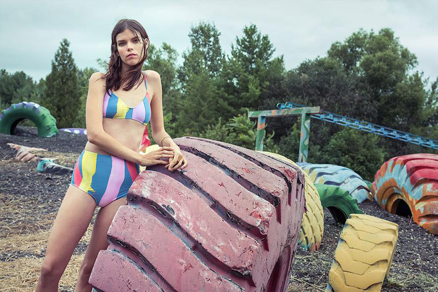 Woman in blue, yellow, and pink bikini leaning on a colorful tire